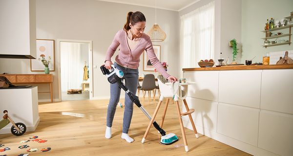 Žena koristi Bosch Unlimited 7 ProHygienic Aqua za brisanje i usisavanje poda u jednom koraku. Ona lako rukuje aparatom oko stolice za hranjenje u kuhinji.