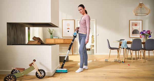 En kvinne rengjør tregulvet i stuen og spisestuen med Bosch Unlimited 7 ProHygienic Aqua.