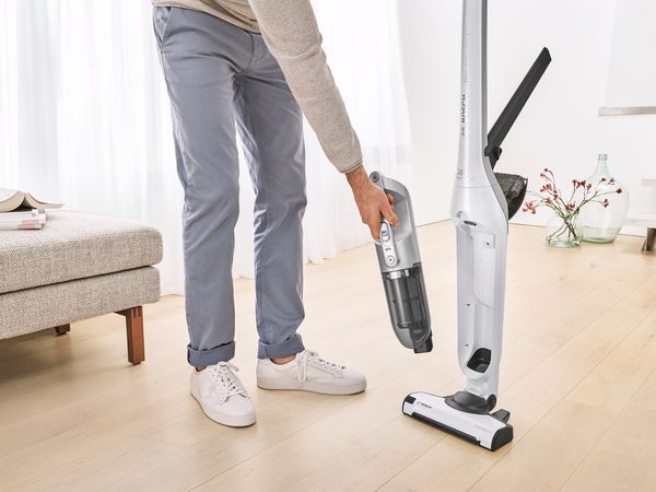 The Flexxo cordless vacuum cleaner has an integrated rechargeable hand vac and other accessories. The appliance is in a living room with a wooden floor.
