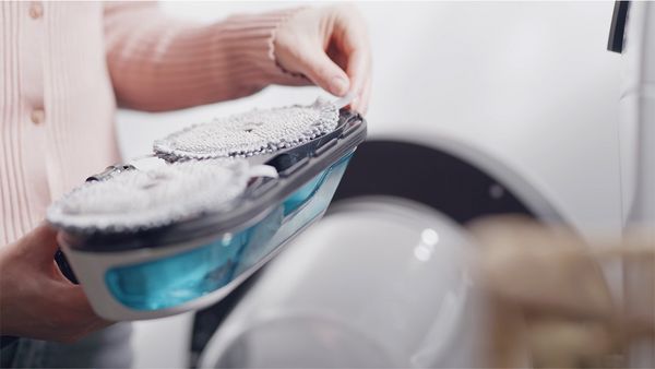 Una mujer retira las almohadillas de microfibra del cepillo 2en1 Dynamic Aqua, listas para lavar.
