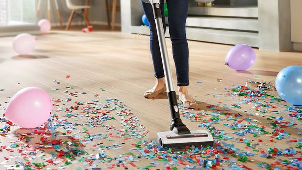 A close up of a cordless vacuum shows how it vacuums confetti of the floor.