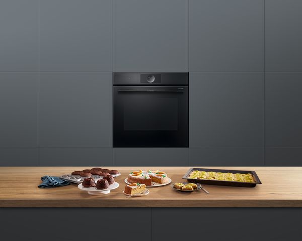 Serie 8 elektrische oven van Bosch in een keuken. Op een werkblad ervoor staat divers gebak, zoals een worteltaart en muffins.