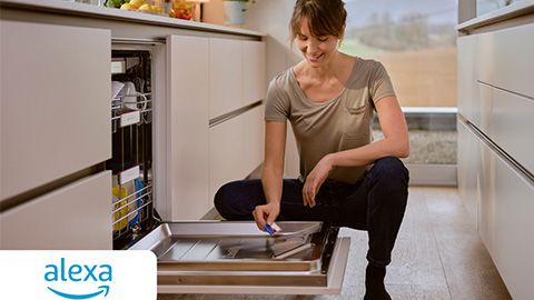 A man and woman in front of their dishwasher by a finish tablet packet