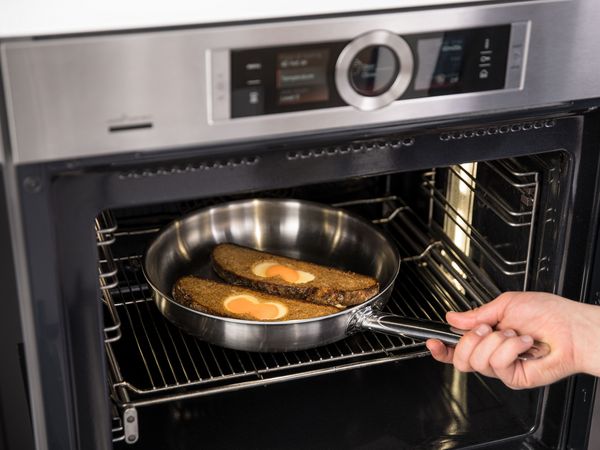 Person putting two slices of sunchine toast in frying pan in oven