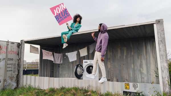 Junge Frau und junger Mann draussen vor einer Wäscheleine und Waschmaschine mit Schriftzug Join Blue Movement.