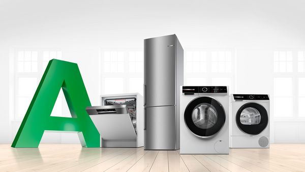 Ein heller, leerer Wohnraum mit einem großen Buchstaben A in grün und einer Spülmaschine, Kühlschrank, Waschmaschine und Trockner.