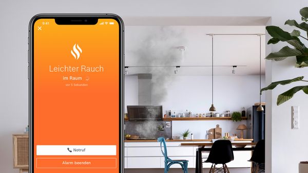 Eine Küche mit einer kleinen Rauchwolke und ein Handy mit der Smart Home App, die eine Warnung zeigt.
