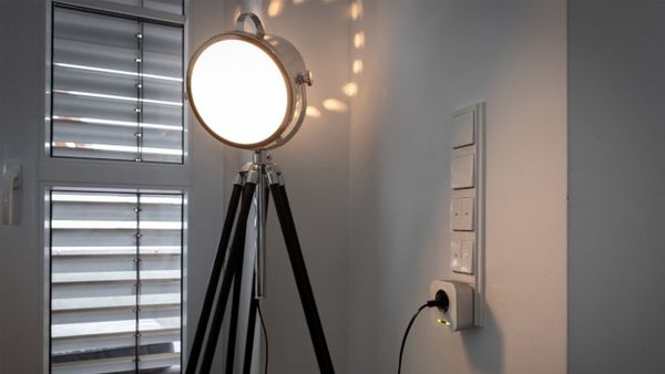 Ein abgedunkeltes Zimmer, in dem eine leuchtende Standlampe an den Smart Home Zwischenstecker angesteckt ist.
