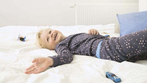 Ein Kind in Pyjamas, das lächelnd im Bett liegt.