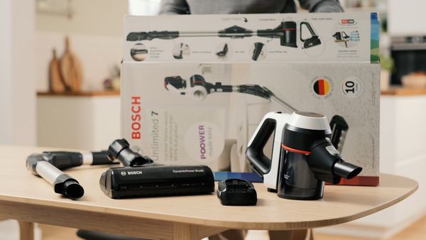 In front of the open package there are nozzle, hose, quick charger and battery vacuum cleaner on the table.