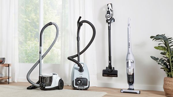 Four different vacuum cleaners are lined up in a bright hallway.