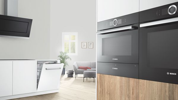 En lyst og åpent kjøkken med møbler i tre og hvitt, fullt utstyrt med Bosch husholdningsapparater.