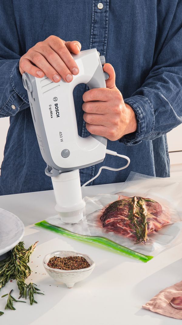 A person connecting a compatible hand mixer to a vacuum bag.