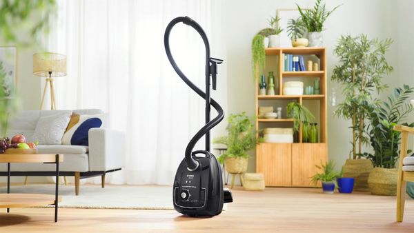 A Bosch cylinder vacuum stands upright in front of a cabinet in a living area.