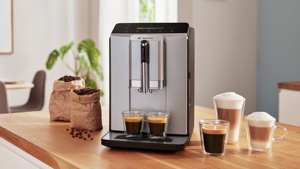 Serie 2 VeroCafe Kaffeevollautomat mit zwei Tassen Espresso auf der Tropfschale, daneben Latte Macchiato, Kaffee und Cappuccino auf der Küchenarbeitsplatte.