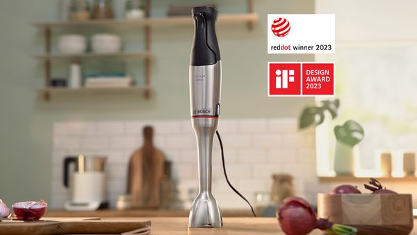 A video still shows the ErgoMaster hand blender and cut fruit on a kitchen counter in front of a sunny window.