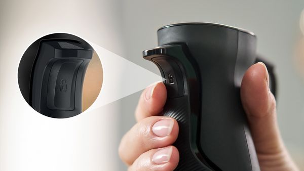 A hand holds the ErgoMaster blender as the index finger rests on the switch, which is shown in more detail in an inset.