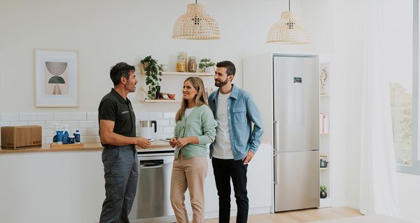 En servicetekniker står på et kjøkken og snakker med en mann og en kvinne.