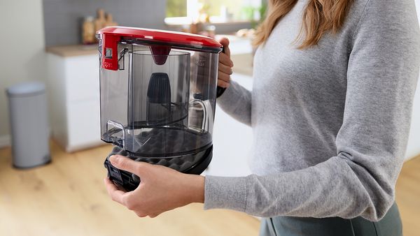 A woman lifts the dust box out from a canister vacuum cleaner.