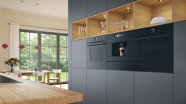 Moderne, dunkelgraue Küche mit Holzregalen und drei schwarzen horizontal eingebauten Hausgeräten.
