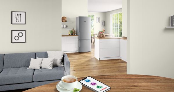 Te og smartphone på et træbord i dagligstuen med hvidt køkken i baggrunden.