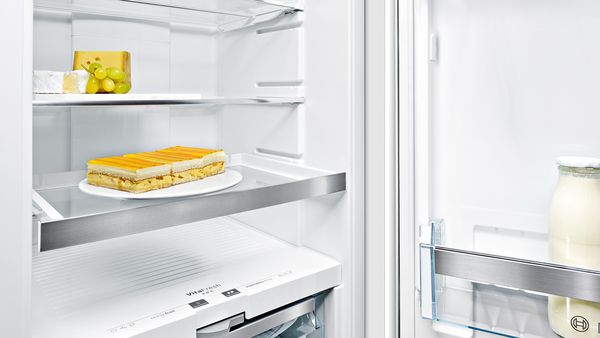 Een close-up van het interieur van een koelkast laat de in hoogte verstelbare schappen van veiligheidsglas zien, met daarop een bord met plakjes cake en andere items.