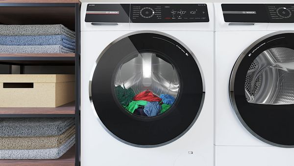 Bosch washing machine with i-Dos automatic dosing placed in a laundry room. Cabinets next to the efficient washing machine with cactus showing a peace sign placed on the cabinet. 