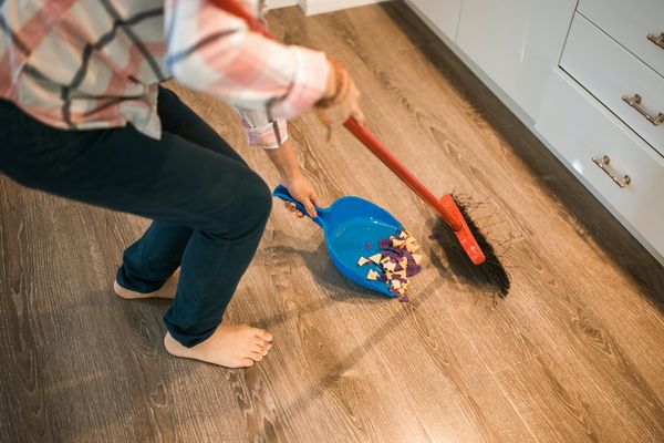 Kobieta za pomocą szufelki i szczotki sprząta zanieczyszczenia z podłogi.