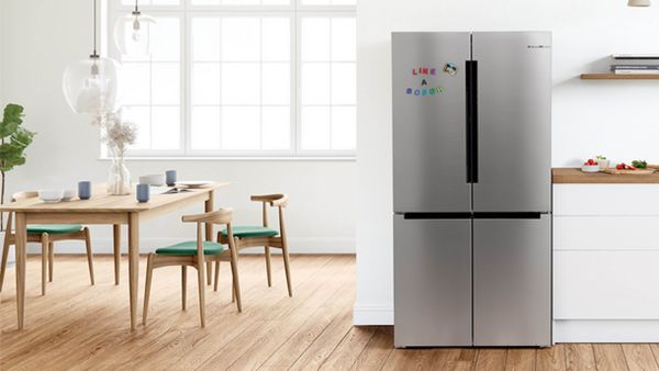 A modern white kitchen, with a silver Bosch XXL fridge freezer just off center of the page. 