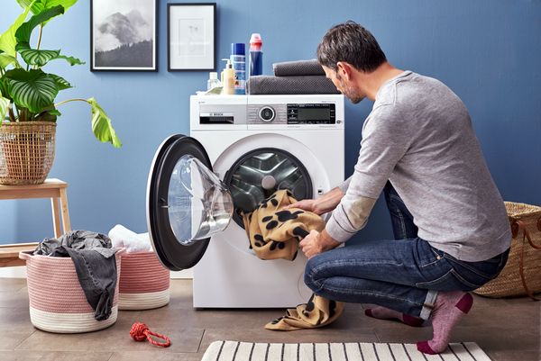 Mann gibt eine Hundedecke in die Waschmaschine, um Hundehaare zu entfernen.