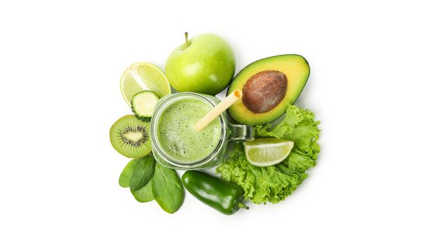 Blenderkan met smoothie gevuld van bovenaf gezien naast groene ingrediënten, waaronder avocado, appel, limoen, kiwi, basilicum en paprika.