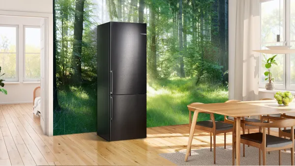 Un frigorifero nero si trova in una cucina luminosa con pavimenti in legno, accanto a un murale di una foresta serena, suggerendo un'atmosfera naturale. 