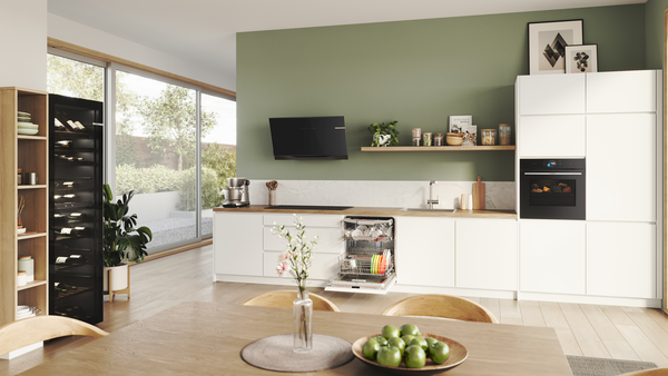 Eine helle Einbauküche mit weißen Möbeln und einer lindgrünen Wand in der moderne Bosch Hausgeräte verbaut sind.