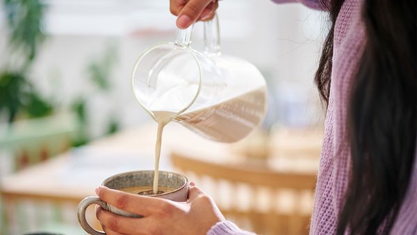 Eine Frau in einem lila Pullover gießt Hafermilch in eine Tasse.