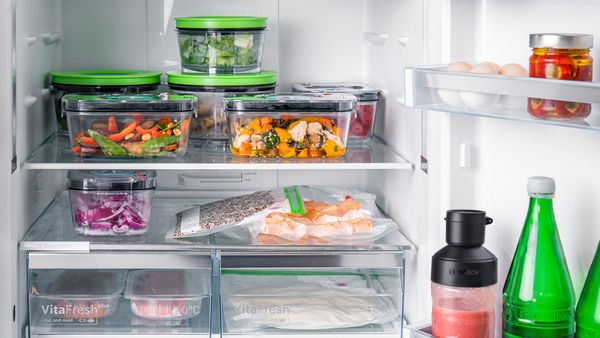 Un réfrigérateur rempli d'aliments frais et cuits, emballés sous vide dans des récipients et des sacs.