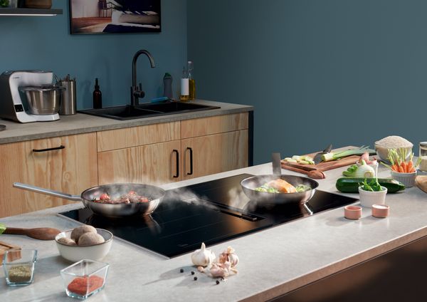 Un uomo in cucina con due padelle su un piano cottura con PerfectFry. Cottura perfetta di carne e pesce.
