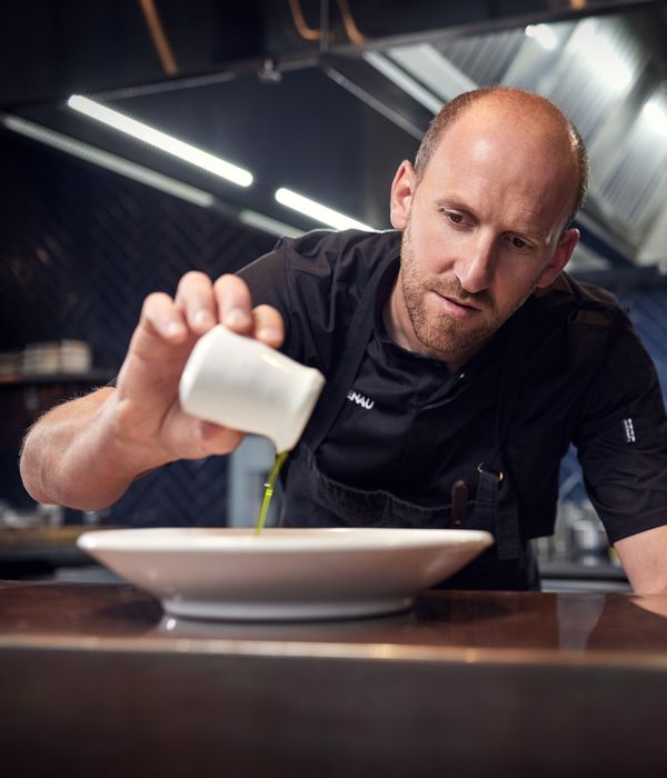 Portrait of Simon Levy pouring oil on a dish created in his restaurant Hali 