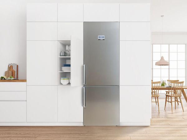 Small one-wall farmhouse kitchen with cream cabinets, a grey-blue backsplash and a compact freestanding stainless steel fridge-freezer fitted close to the side wall