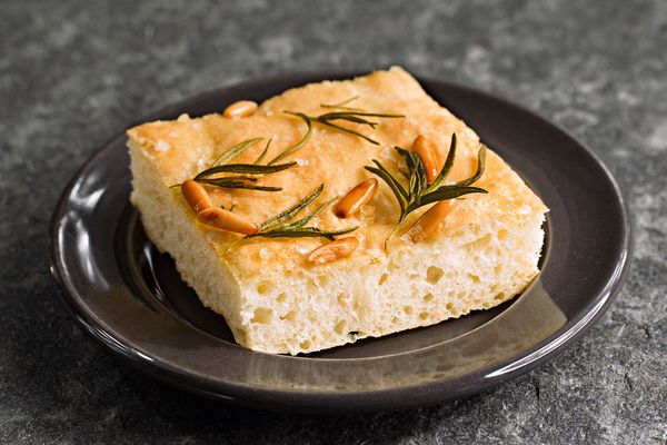 Focaccia soffice con rosmarino e pinoli servita su un piatto scuro