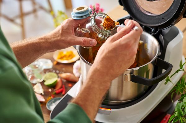 Eine Person gibt Currypulver in eine Bosch Cookit Küchenmaschine