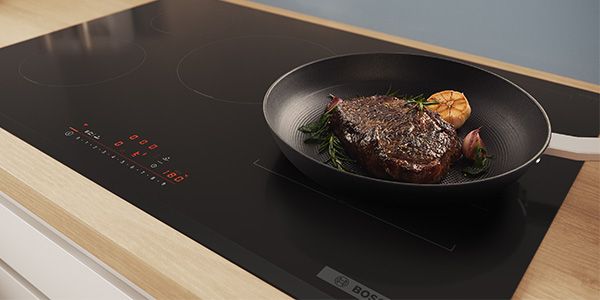 Un steak avec des gousses d'ail en train de frire dans une poêle sur une table de cuisson à induction.