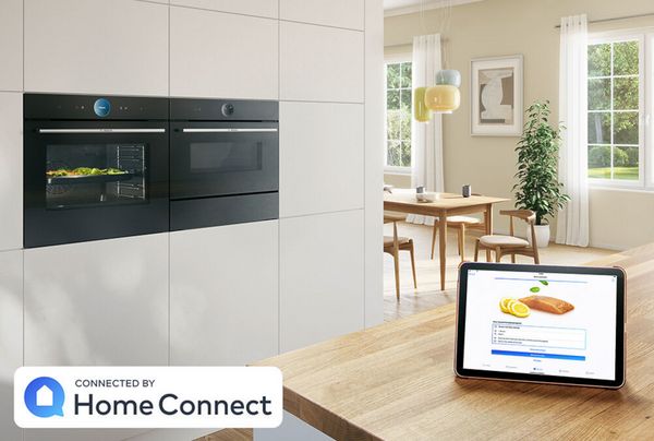 Elegante Küche mit eingebautem Serie 8 Elektrobackofen sowie Wärmeschublade und ein Tablet auf der Arbeitsplatte zeigt die Home Connect App.