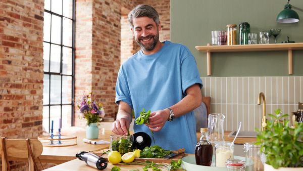 Ein mittelalter Mann befindet sich in einer Küche und ist dabei, ein Pesto zuzubereiten.