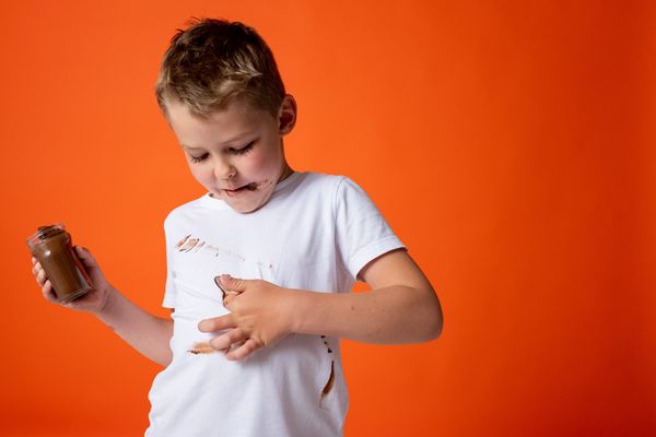 Chłopiec z plamami czekolady na białej koszulce na pomarańczowym tle
