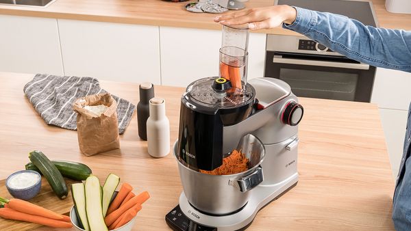 Eine Person nutzt die Bosch Küchenmaschine, um eine Karotte zu schneiden