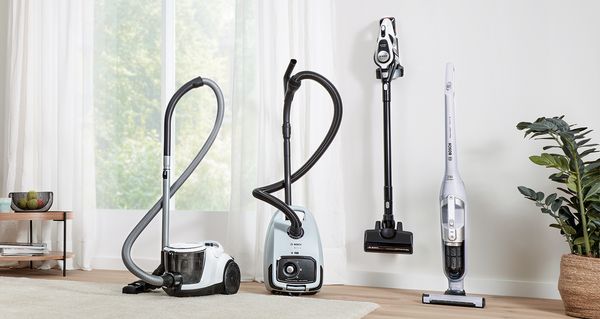 Various different Bosch vacuums are lined up in front of a wall and window in a living area.