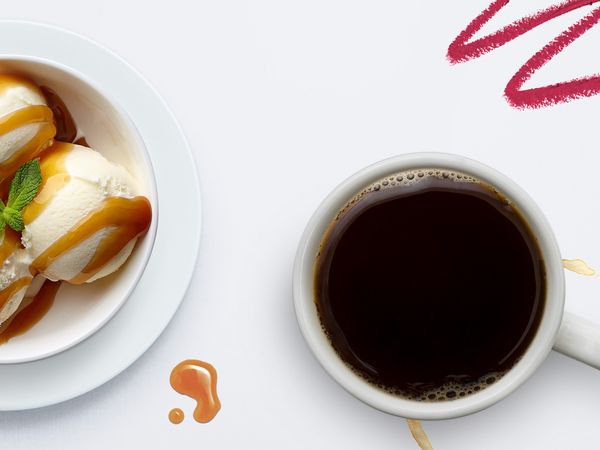 Flecken von einer Schale Eiscreme, einer Tasse Kaffe und einem Lippenstift auf einer weißen Tischdecke.