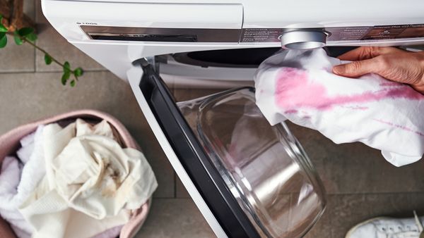 Eine Person legt ein fleckiges weißes Kleidungsstück in eine geöffnete Waschmaschine.