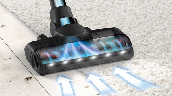 A close-up of a floorhead positioned where carpet meets hard floor. Arrows show how the dirt is pulled into nozzle and up the tube.