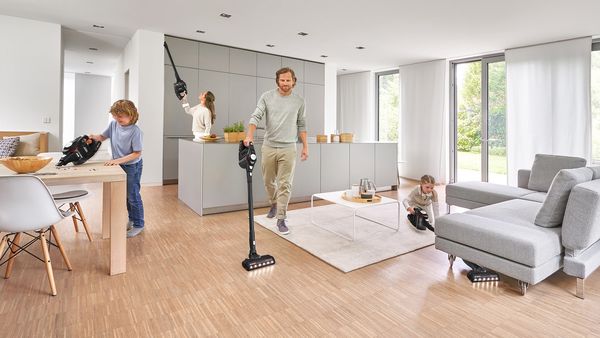 Czteroosobowa rodzina używająca odkurzacza Unlimited do sprzątania wszystkich poziomów – gzymsów, stołów i podłóg – w otwartym salonie.